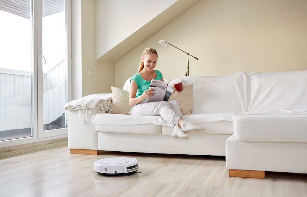 Robot vacuum on hardwood floor with woman in background